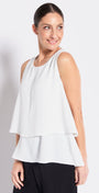 Woman wearing a white sleeveless top with a layered design on a plain background