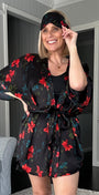 A woman wearing a black short-sleeve robe with a red floral pattern and tan slippers, posing in a modern living room setting.