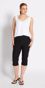 A woman modeling a white sleeveless V-neck top and black cropped pants against a plain white studio background.