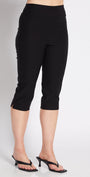 A woman modeling black capri pants with a white cropped tank top and black heeled sandals, posing against a light gray studio background.
