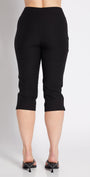 A woman shown from the back wearing black capri pants, a white tank top, and black pointed heels against a plain light gray studio background.