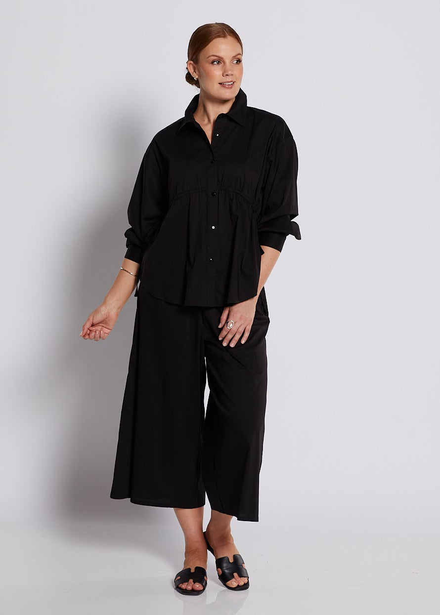 Person wearing a black outfit standing against a white background