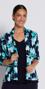 A woman modeling a navy blue cropped pants set with a navy and turquoise floral print blazer, a black top, and silver heeled sandals against a light gray studio background.