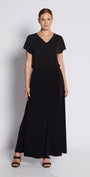 A woman modeling a black short-sleeve maxi dress with a V-neckline, standing against a plain light gray studio background.