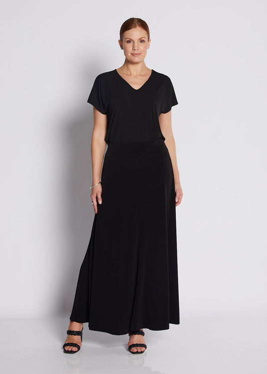 A woman modeling a black short-sleeve maxi dress with a V-neckline, standing against a plain light gray studio background.