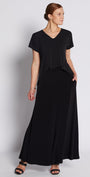 A woman modeling a black short-sleeve maxi dress with a V-neckline and side pockets, standing against a light gray studio background.