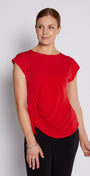 A woman modeling a bright red short-sleeve top with a draped, gathered front detail, paired with black pants, against a light gray studio background.