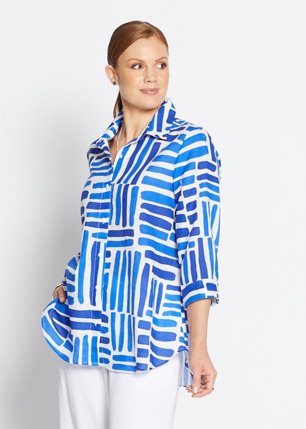 Woman wearing a blue patterned shirt and white pants on a white background