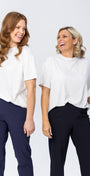 Two women wearing white tops and navy pants standing against a white background