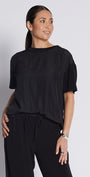A woman modeling a black short-sleeve top and matching black wide-leg drawstring pants, paired with black slide sandals, against a light gray studio background.
