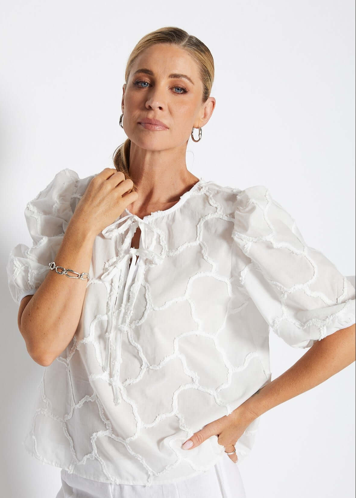 Woman wearing a white dress with ruffled sleeves against a plain background