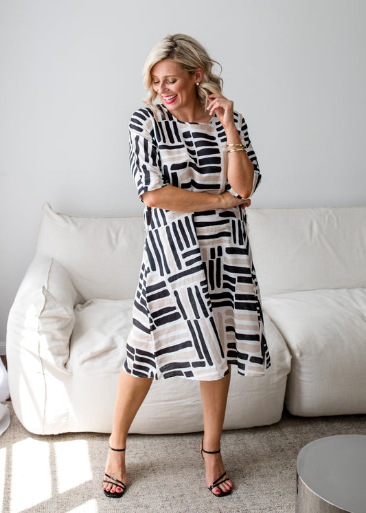 Woman wearing a black and white patterned dress standing in a living room.