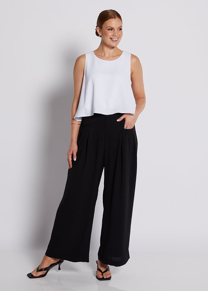 Woman wearing a white sleeveless top and black wide-leg pants against a plain background