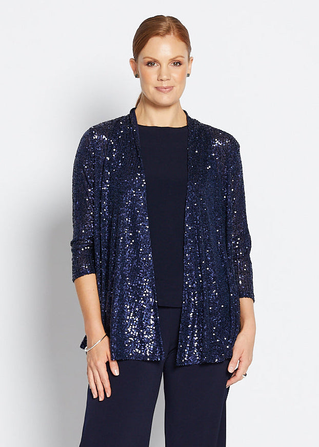 Woman wearing a navy sequin jacket, navy top, and wide-leg pants on a white background