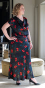 Woman wearing a black dress with red floral patterns in a room.