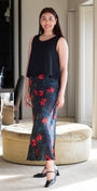 Woman in a black sleeveless top and floral skirt standing in a room with a mirror and furniture.