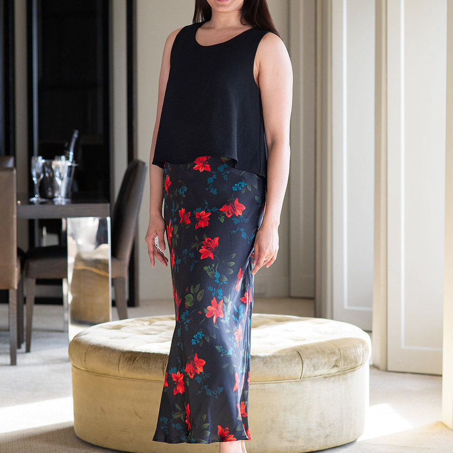 Woman in a black sleeveless top and floral skirt standing in a room with a mirror and furniture.