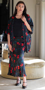 Woman wearing a floral dress and cardigan in a room with a mirror and furniture.
