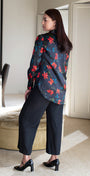 Woman in a floral blouse and black pants standing in a modern room.