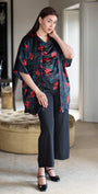Woman wearing a dark floral kimono-style garment in a room with neutral decor.