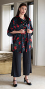 Woman wearing a floral kimono-style top and black pants in a modern room.
