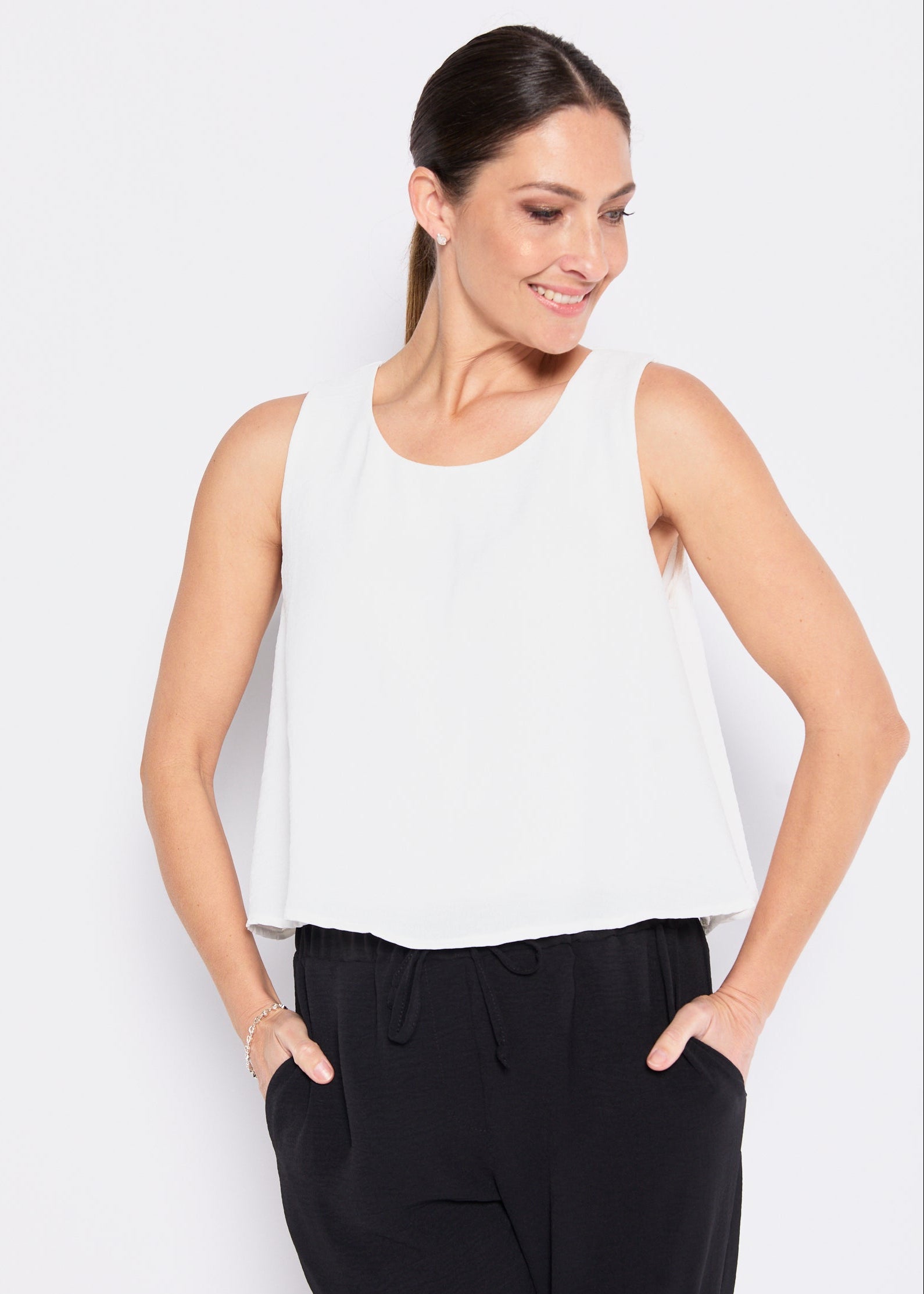 Woman wearing a white sleeveless top and black pants on a white background