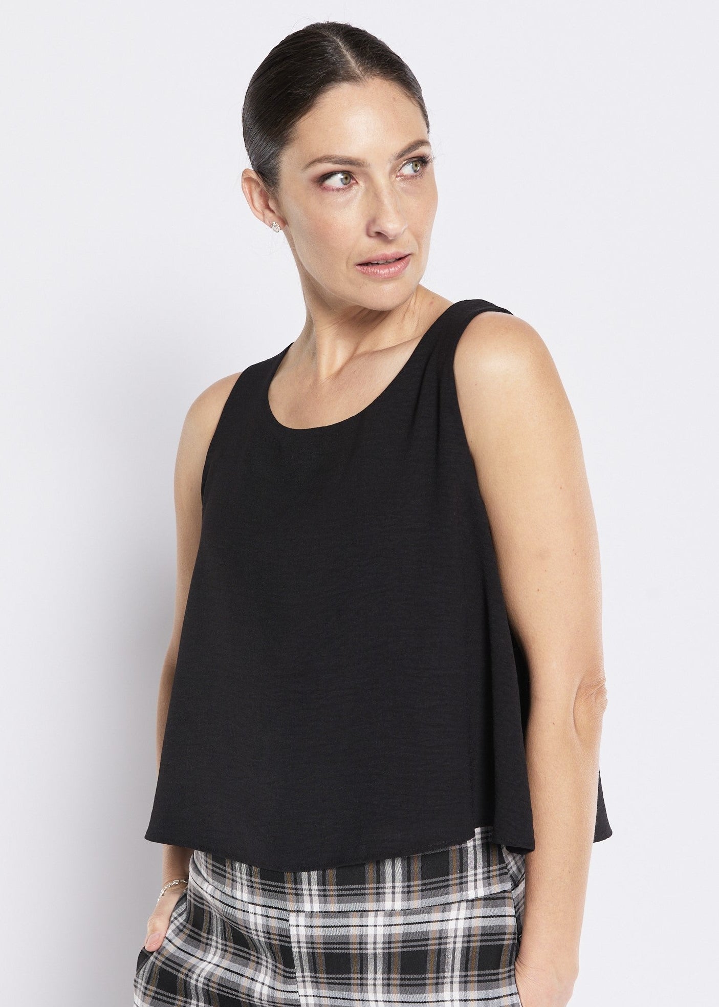 Woman wearing a black sleeveless top and plaid pants against a white background