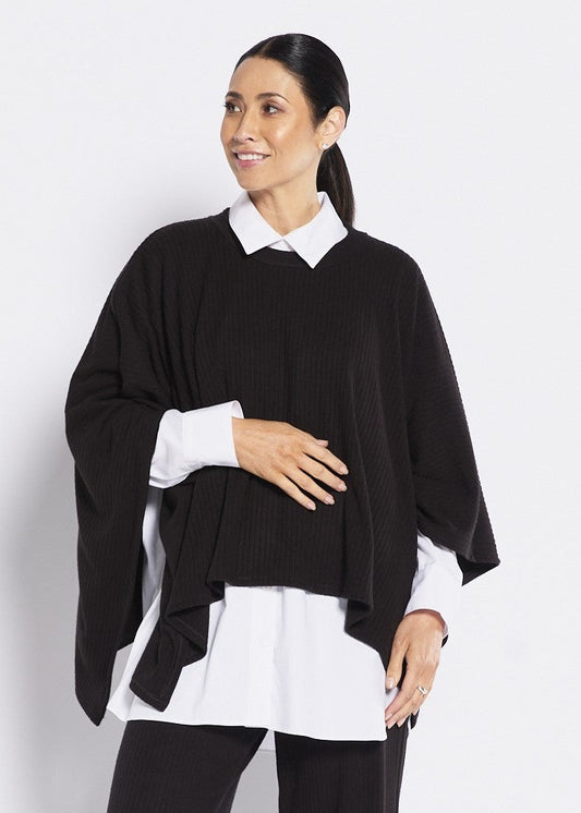 Woman wearing a black poncho over a white shirt and black pants on a white background
